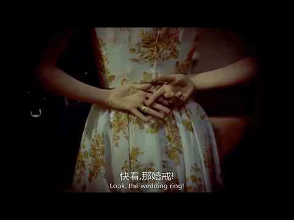 浅色花裙前，一只手的无名指戴着戒指，另一只手指向它；画面下方带中英文硬字幕。